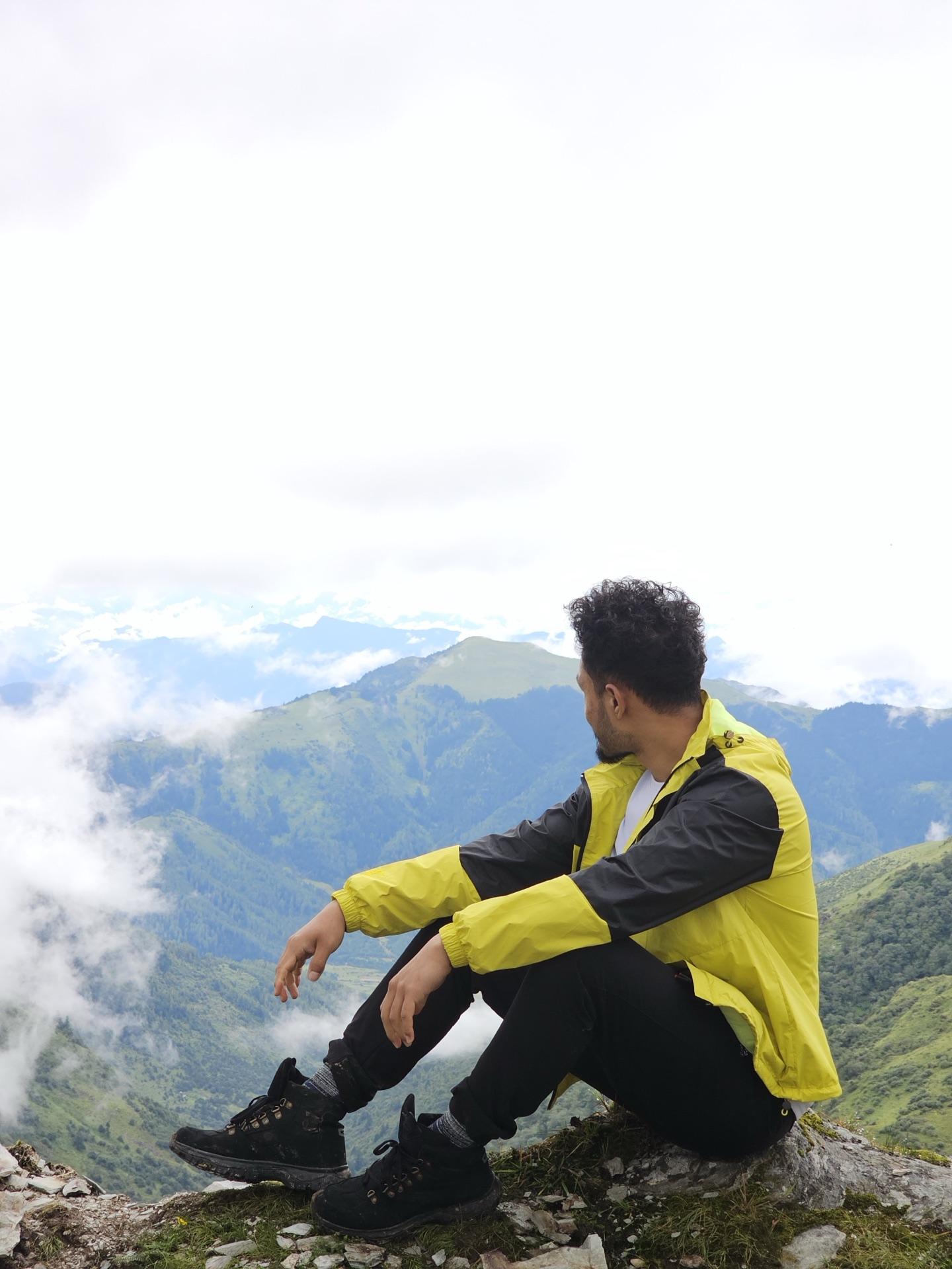 A friend in a yellow jacket sitting on the meadow's edge above a cloud-filled valley