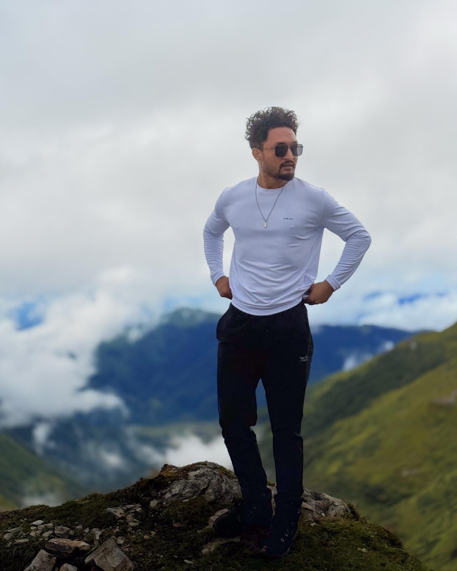 A friend in a white long-sleeve standing hands on hips above the cloud-filled valley