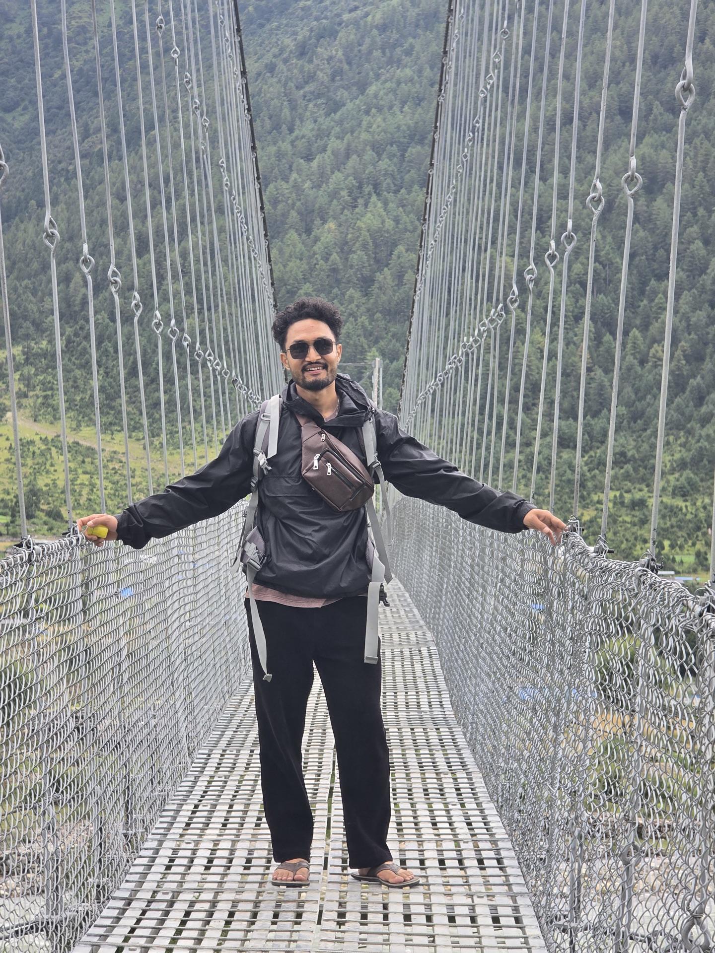 A friend smiling mid-way across a long suspension bridge, wearing chappals