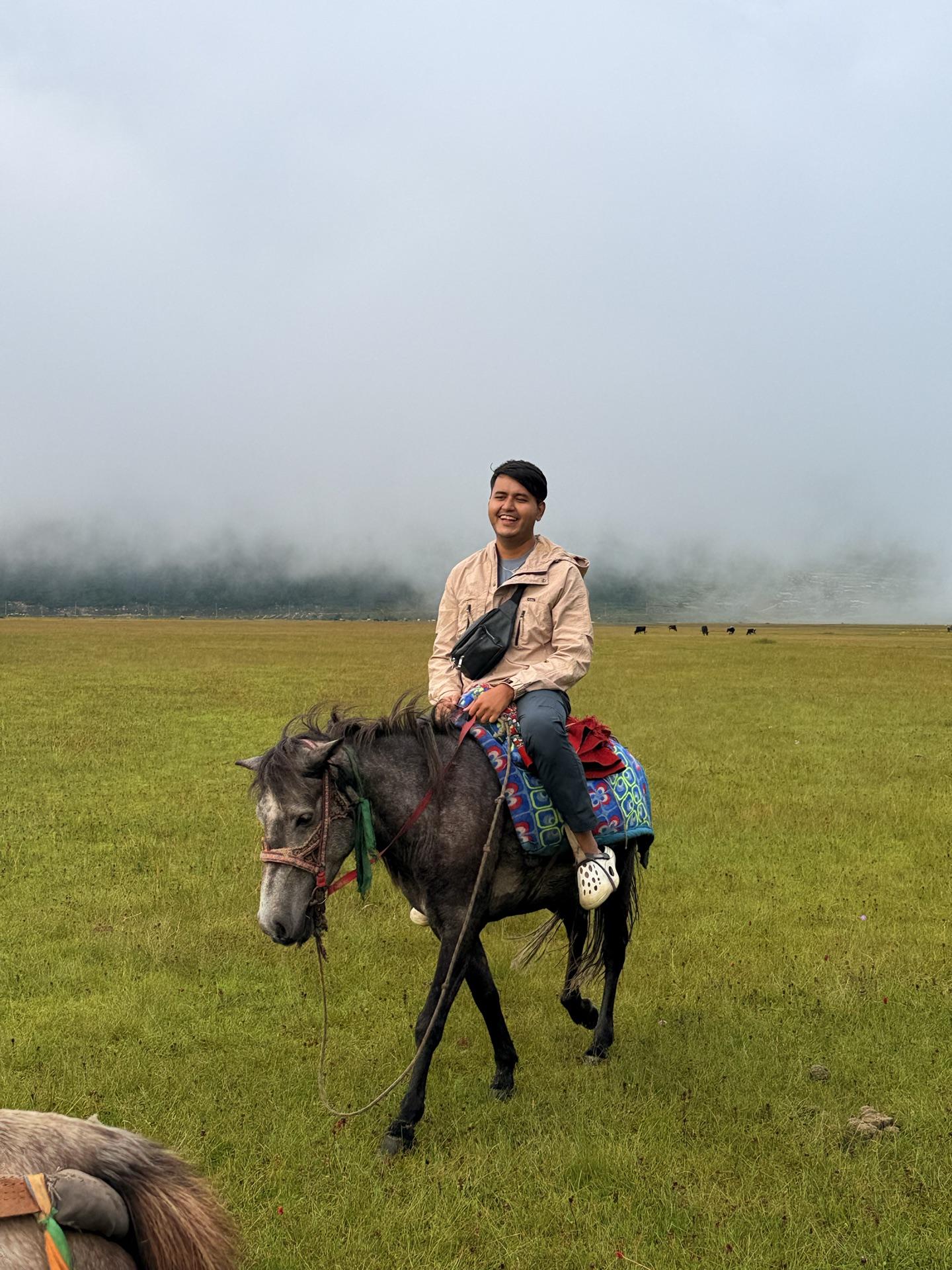 A friend in a cream jacket riding a grey horse across the pasture