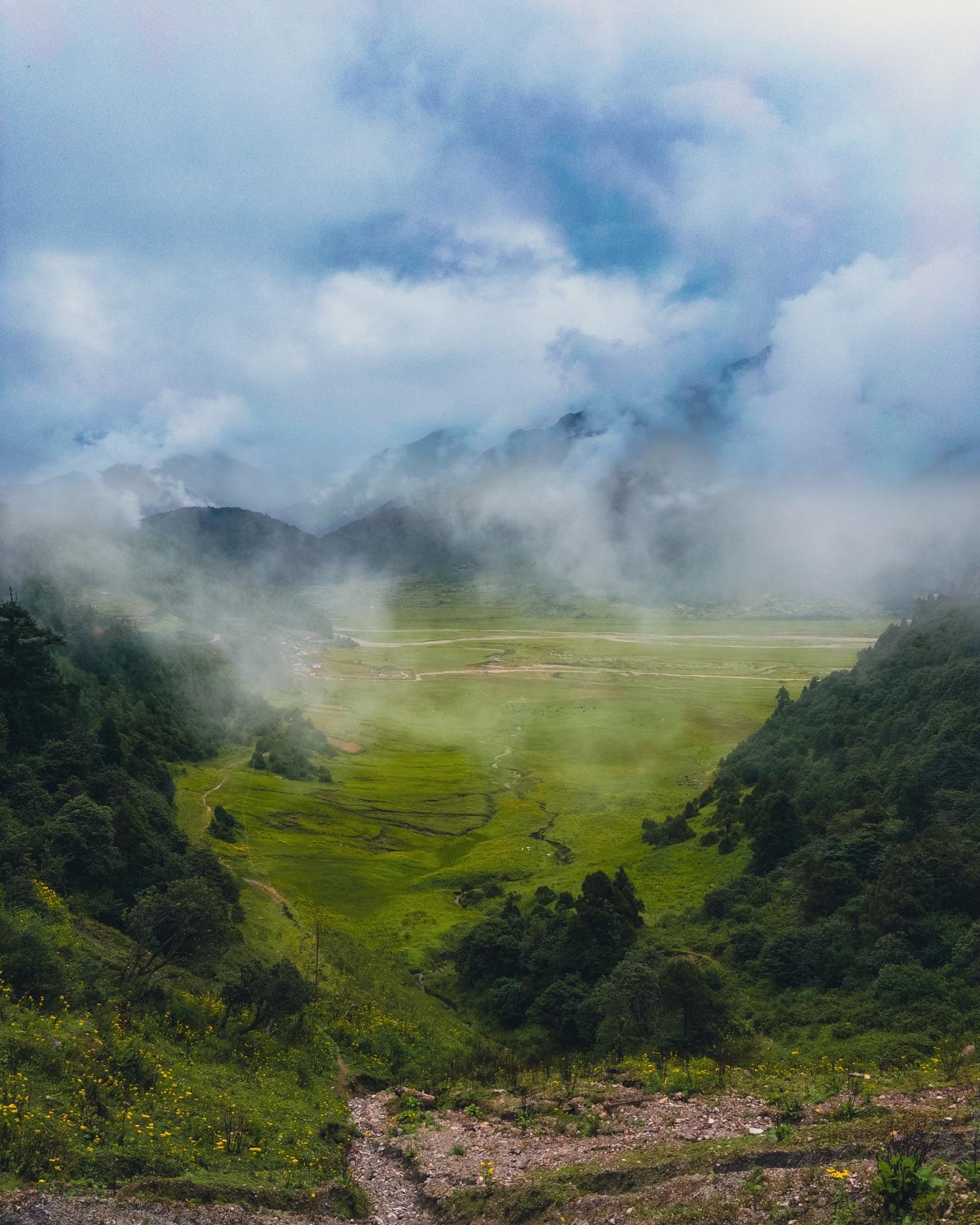 The wide green valley floor appearing below drifting monsoon cloud