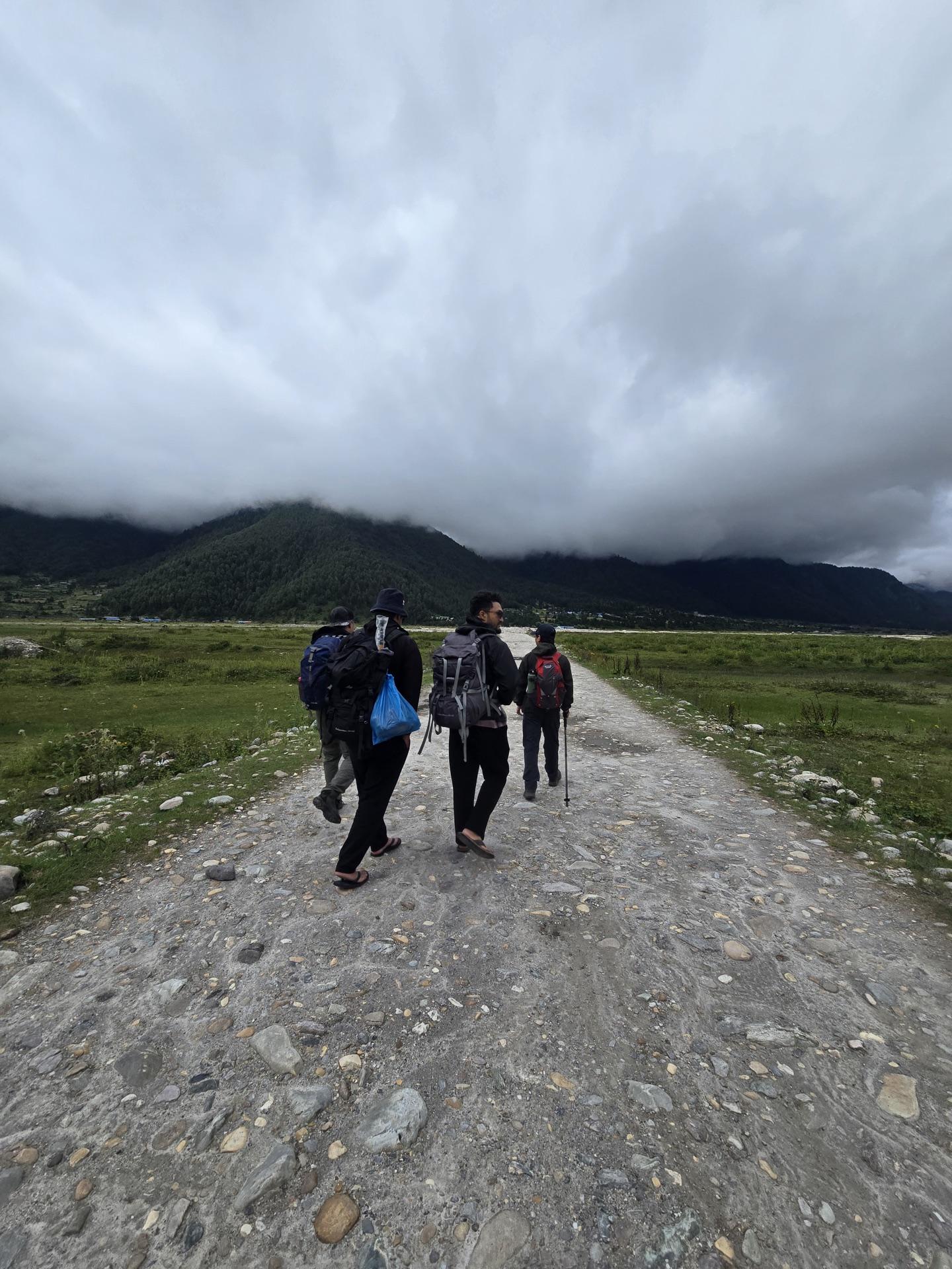 Four friends walking a straight gravel road across the open valley under a heavy sky