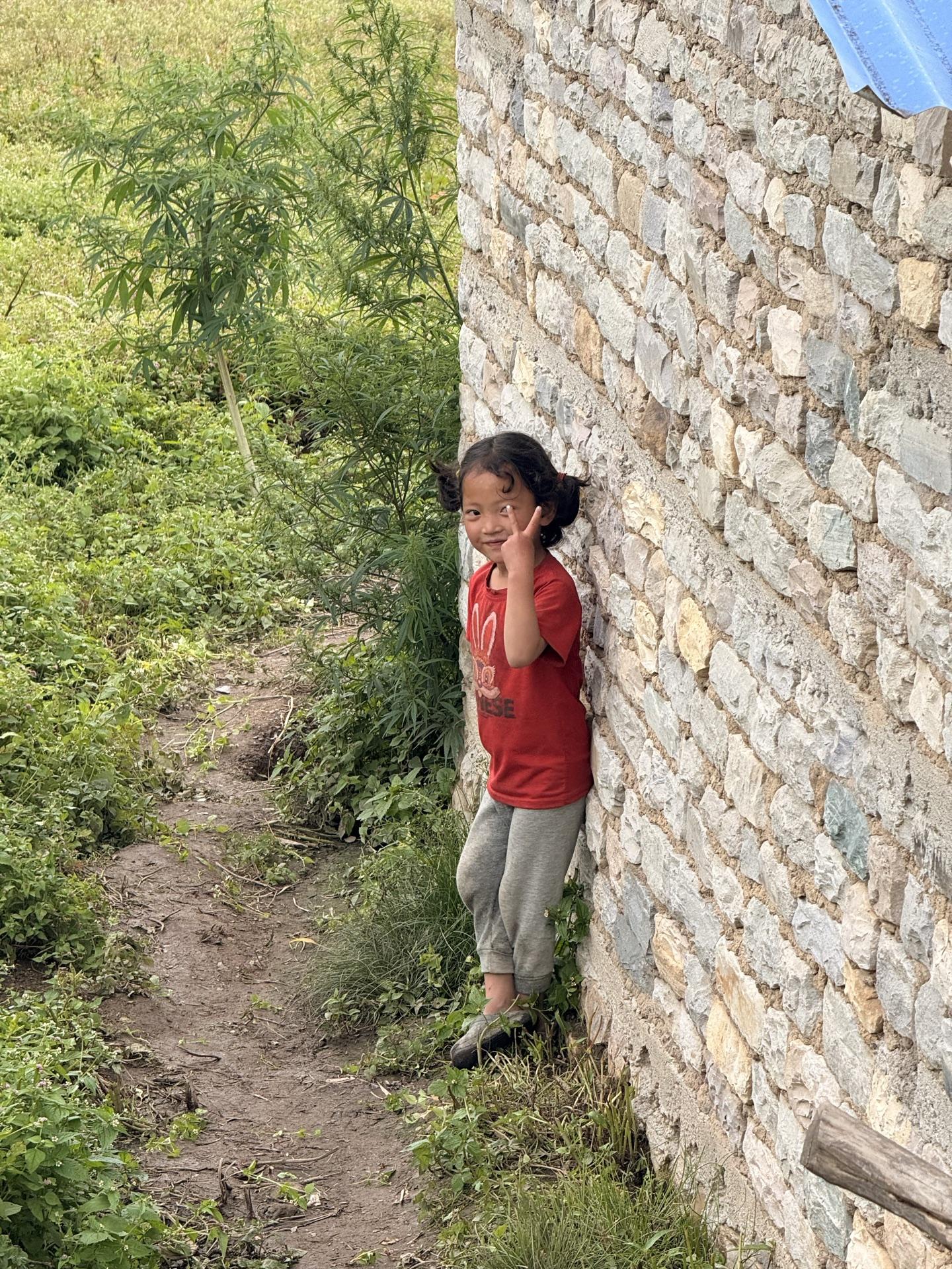 A young girl in red peeking around a stone wall beside the trail