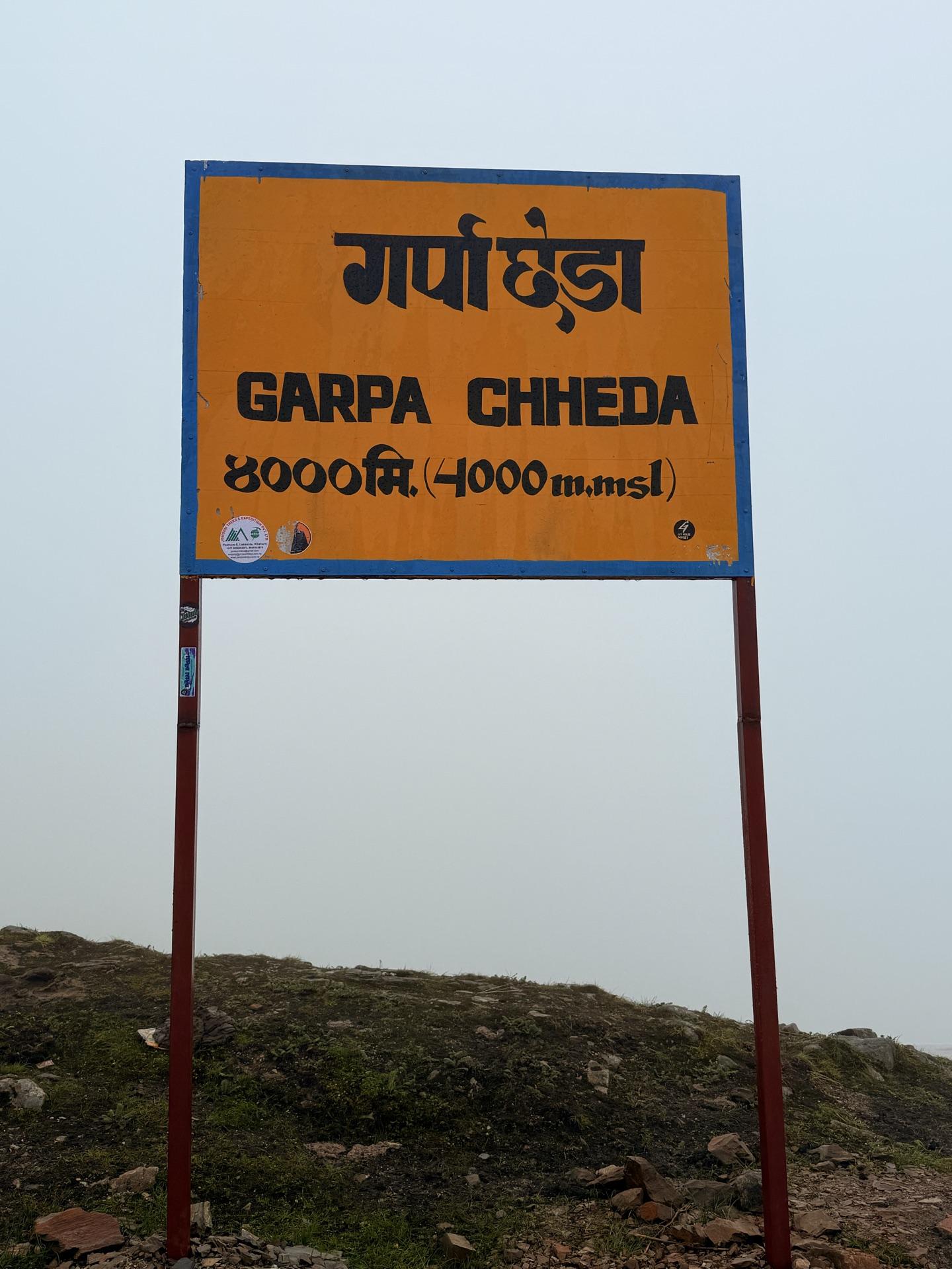 An orange signboard reading Garpa Chheda, 4000 m, standing in the fog
