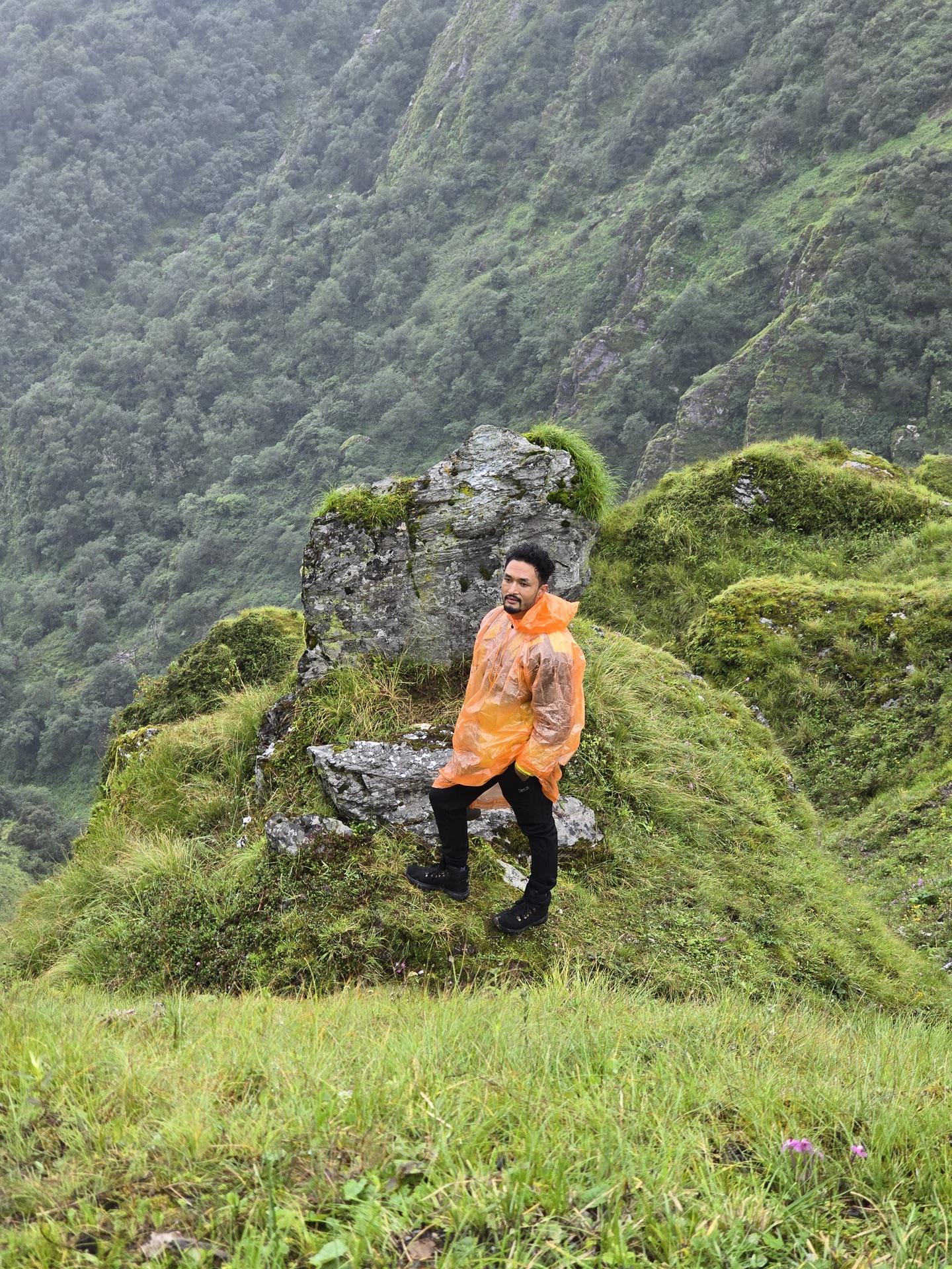 A friend in an orange poncho standing on a lush green ridge in the rain