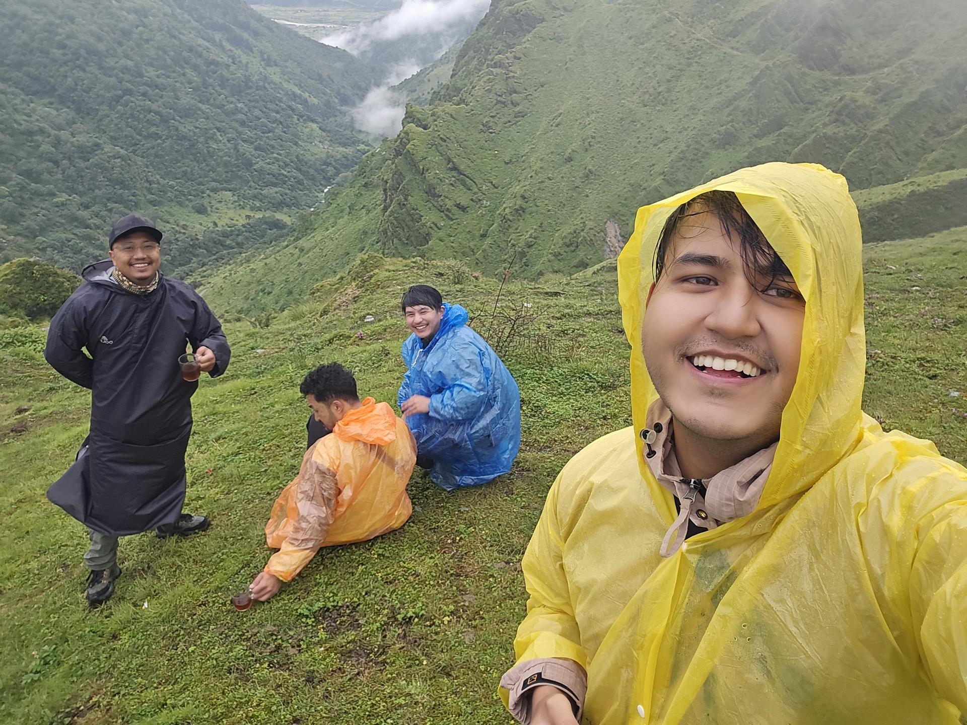 Selfie of grinning friends in ponchos on the green mountainside