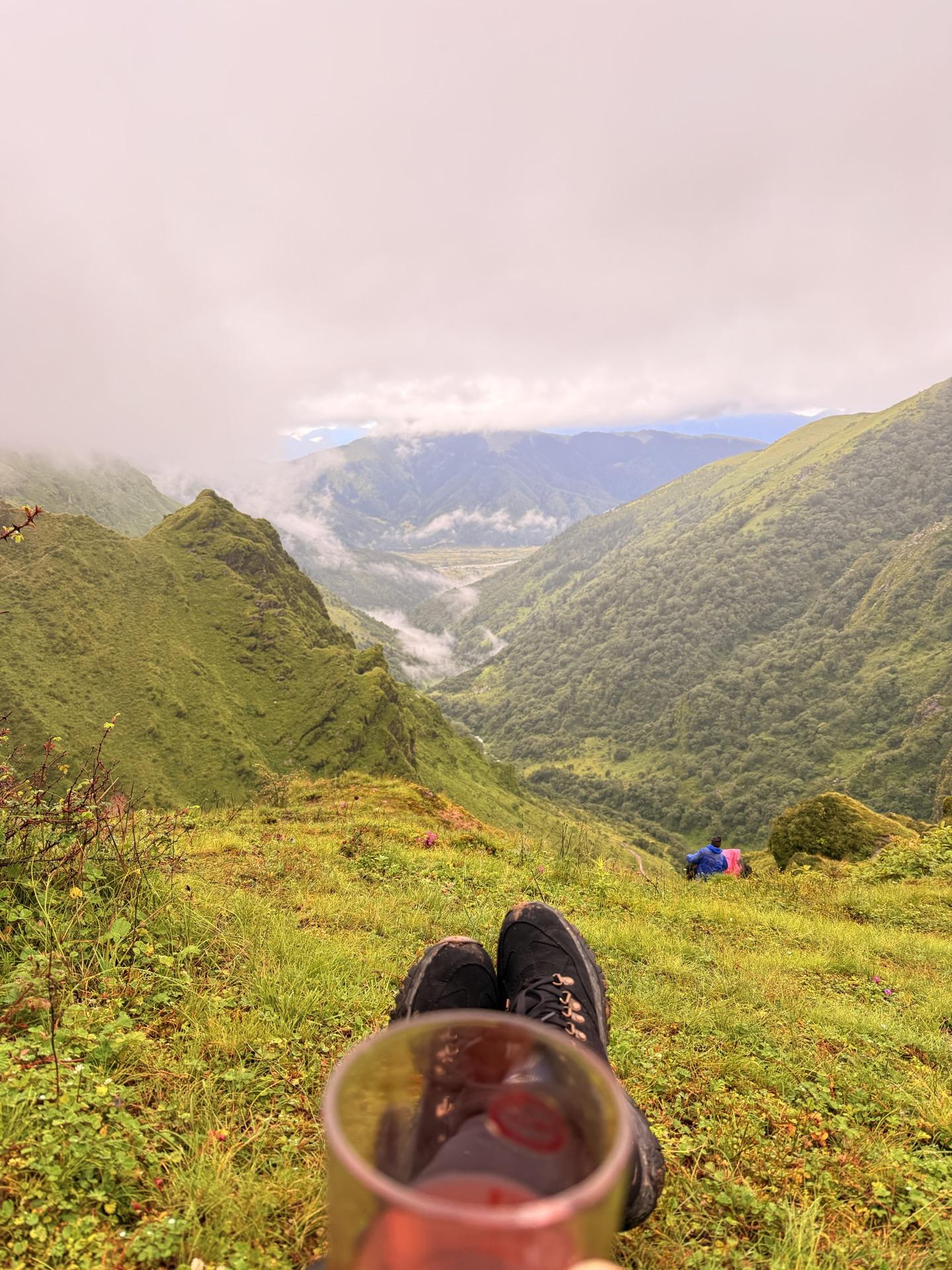 A red cup of tea and a boot in the foreground, the valley falling away in cloud below