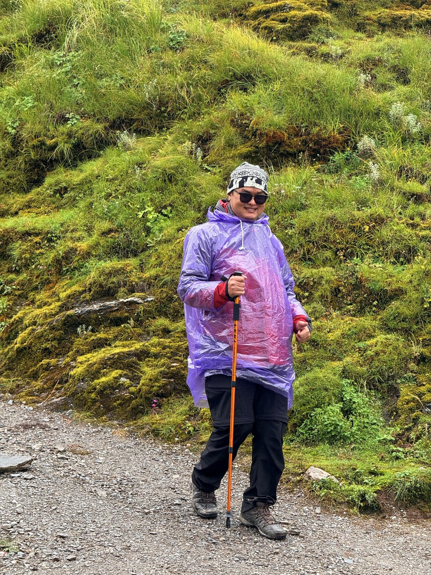 A friend in a purple poncho with a walking stick grinning beside the trail