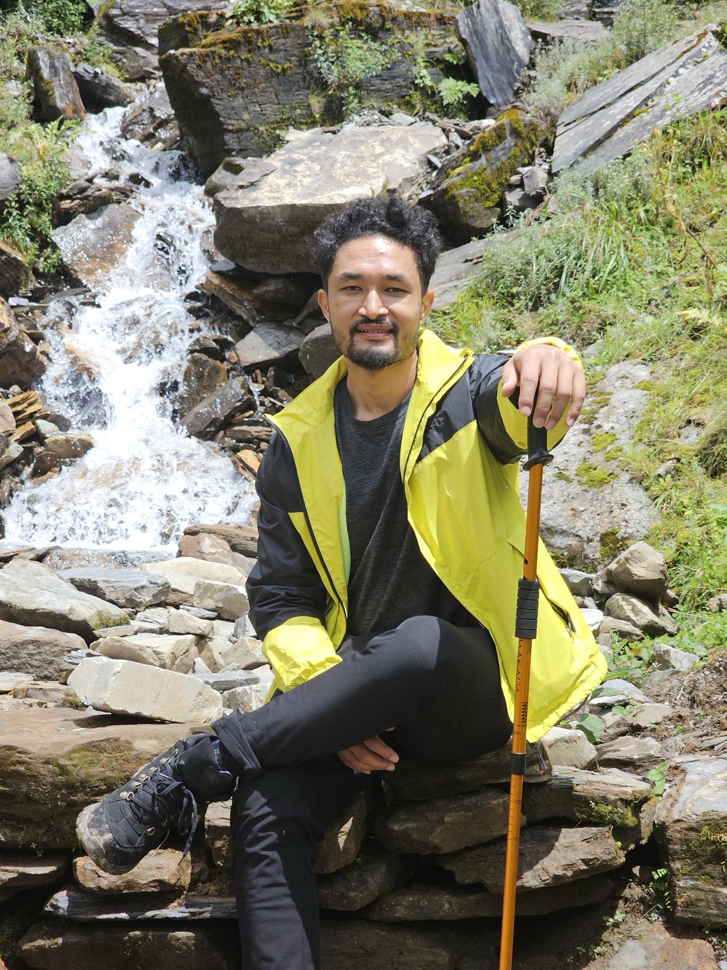 A friend in a yellow jacket sitting on rocks beside a full waterfall