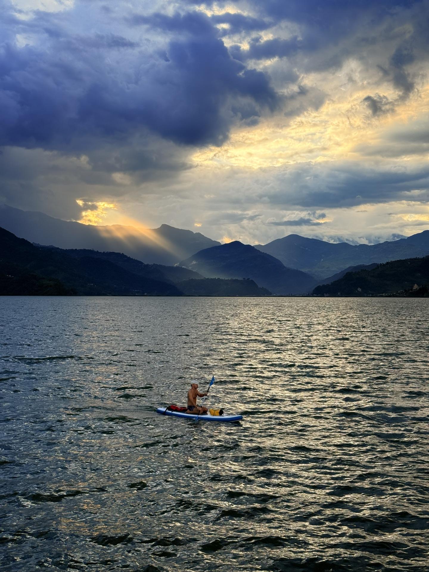 A lone paddleboarder on the silver water of Phewa under god-rays