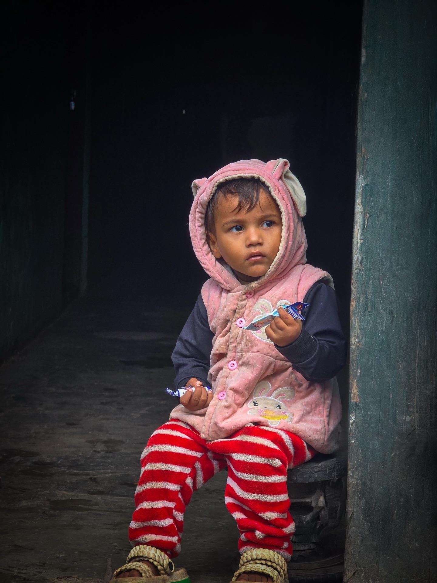 A small kid in a pink hoodie sitting in a dark doorway, seen from the van