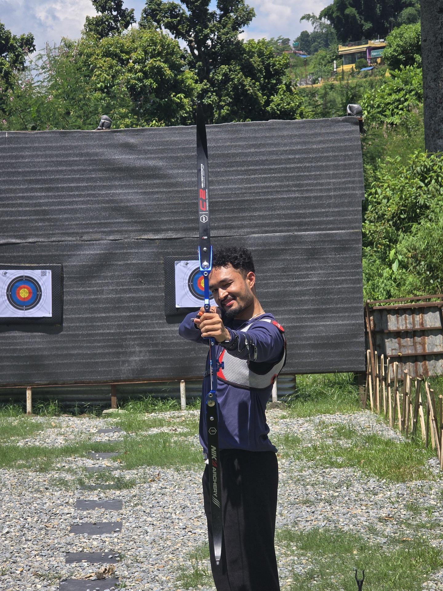 A friend at the archery range holding a bow and giving a thumbs up