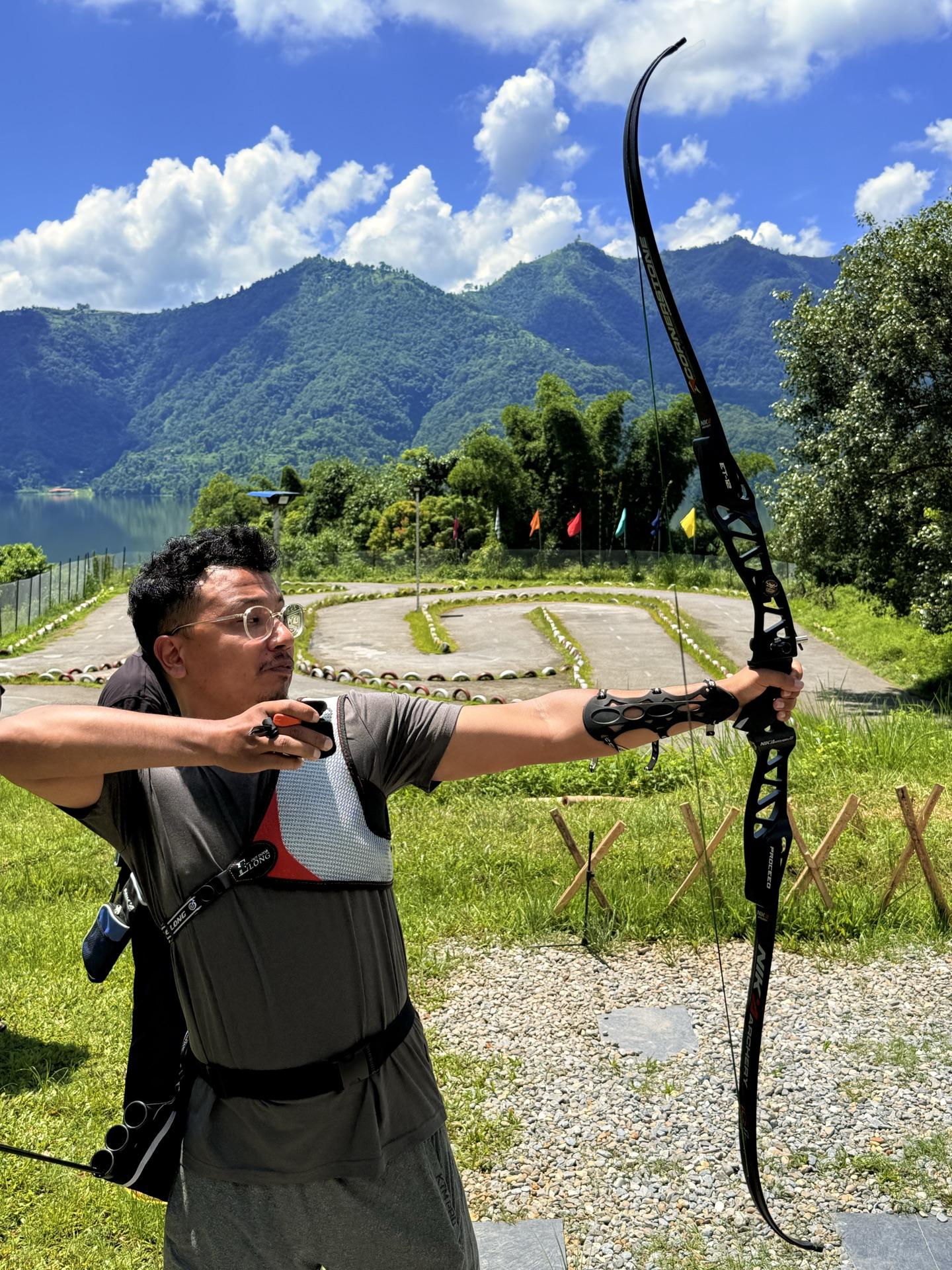 A friend at full draw with the kart track and lake hills behind