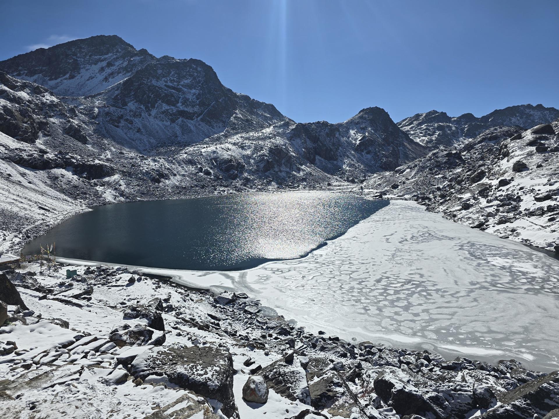 Gosaikunda half-frozen, deep blue water against the white ice sheet, snow to the shoreline