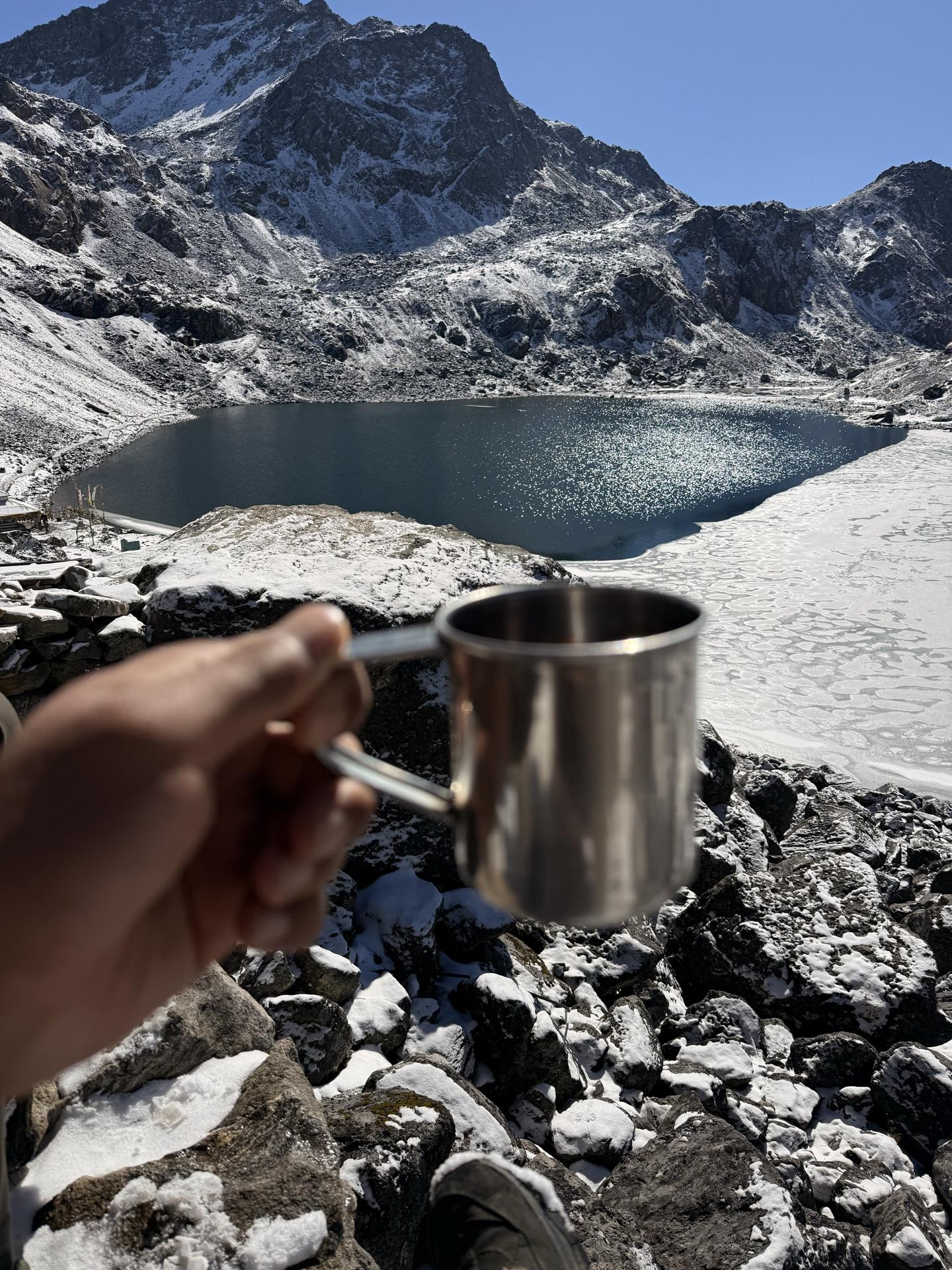 A steel cup of tea raised toward the half-frozen lake
