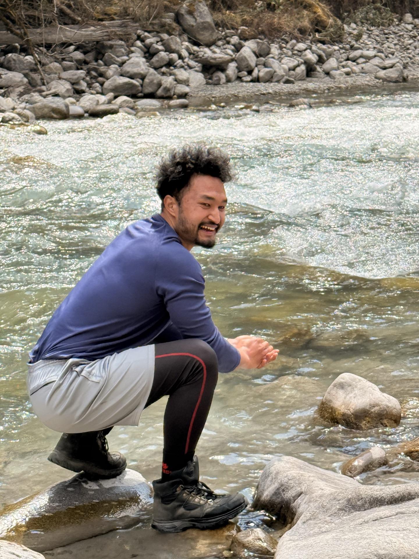 Raju crouched on river rocks splashing glacier water on his face