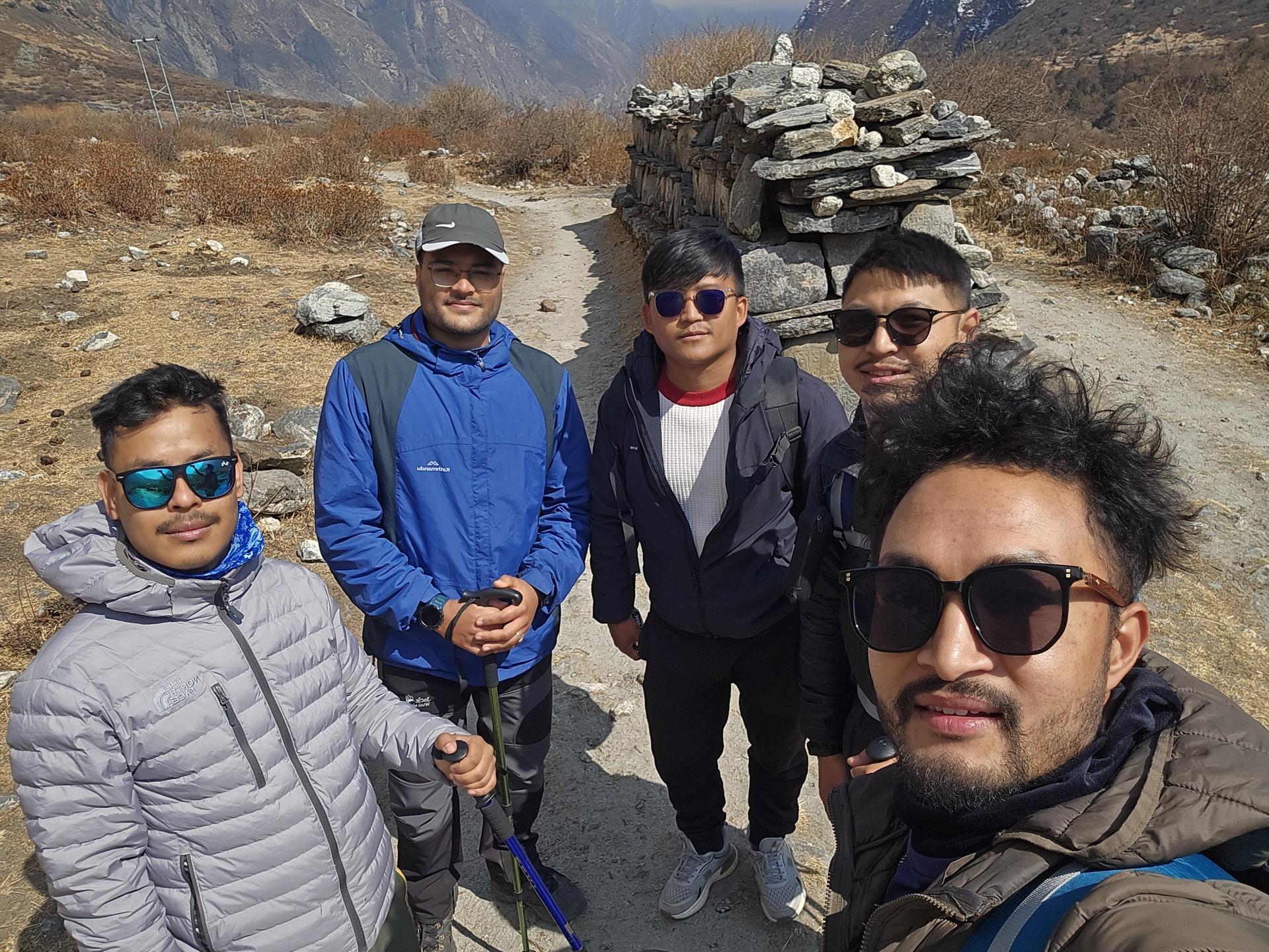 Five trekkers posing together in the open upper valley, snow peaks behind