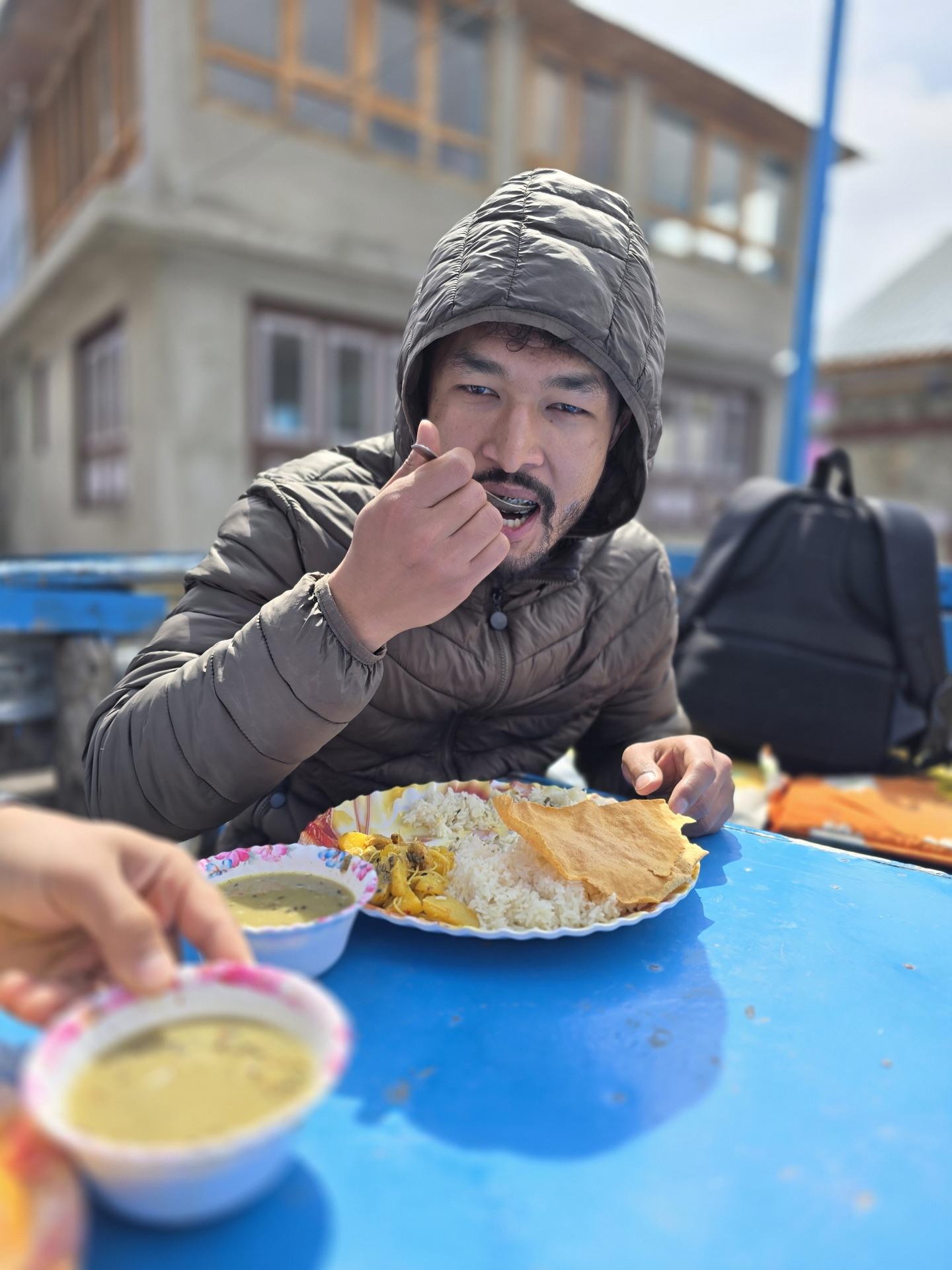 A friend eating dal bhat at a blue table in the sun