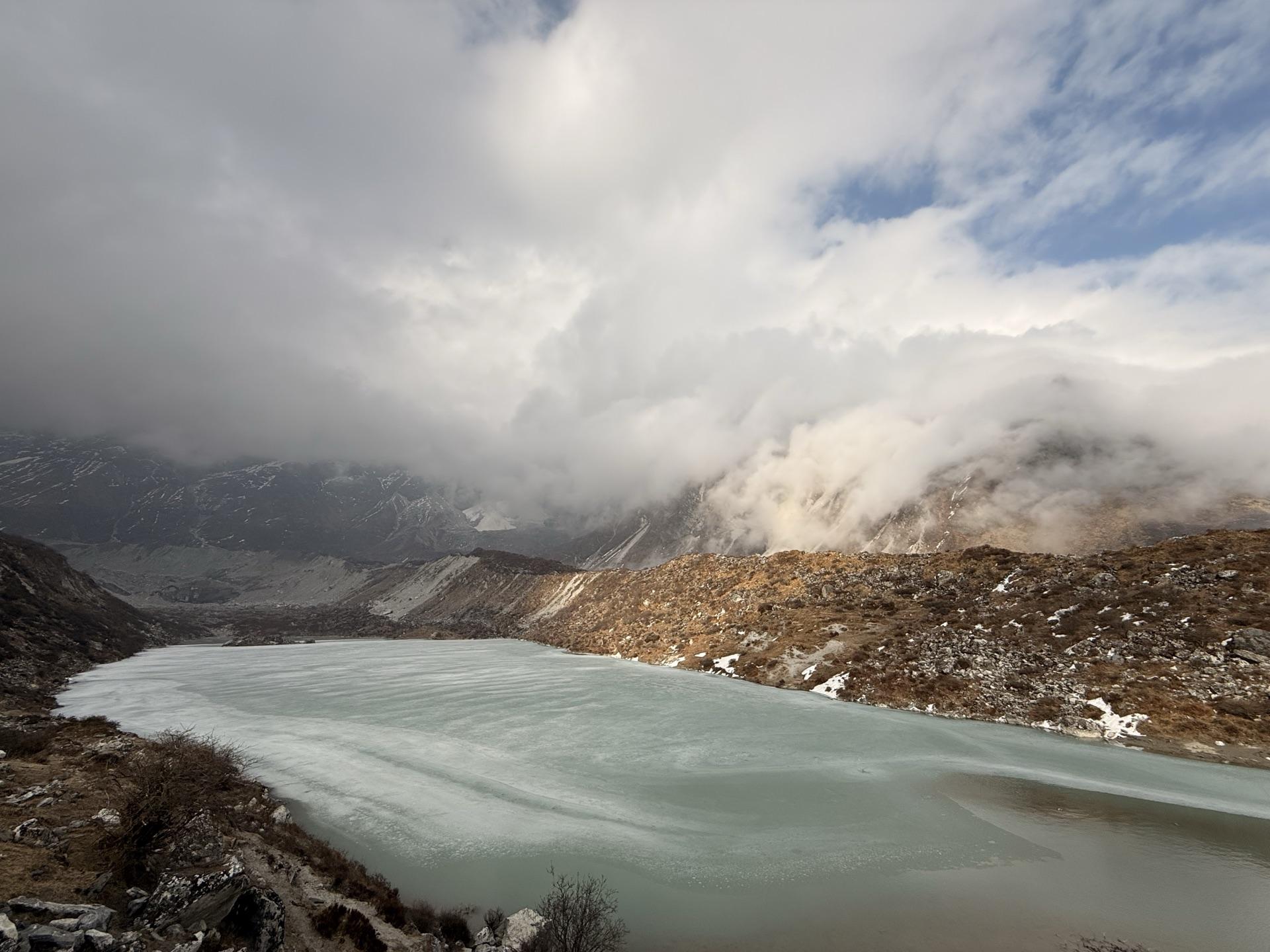 The frozen glacier lake turquoise under cloud-wrapped ridges