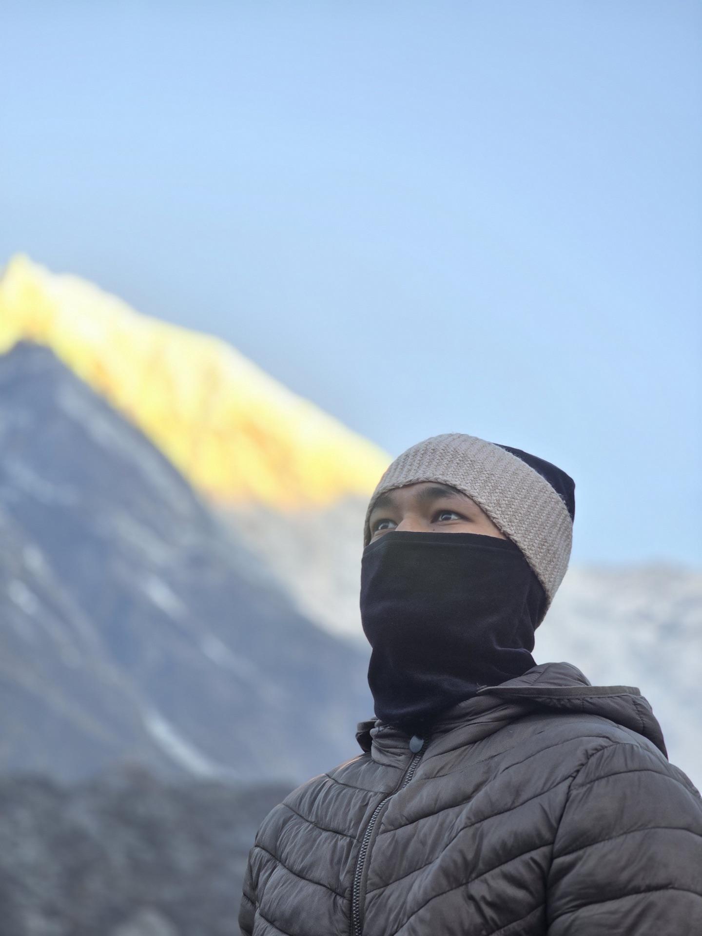 A friend in a balaclava with the summit of Langtang Lirung catching gold light