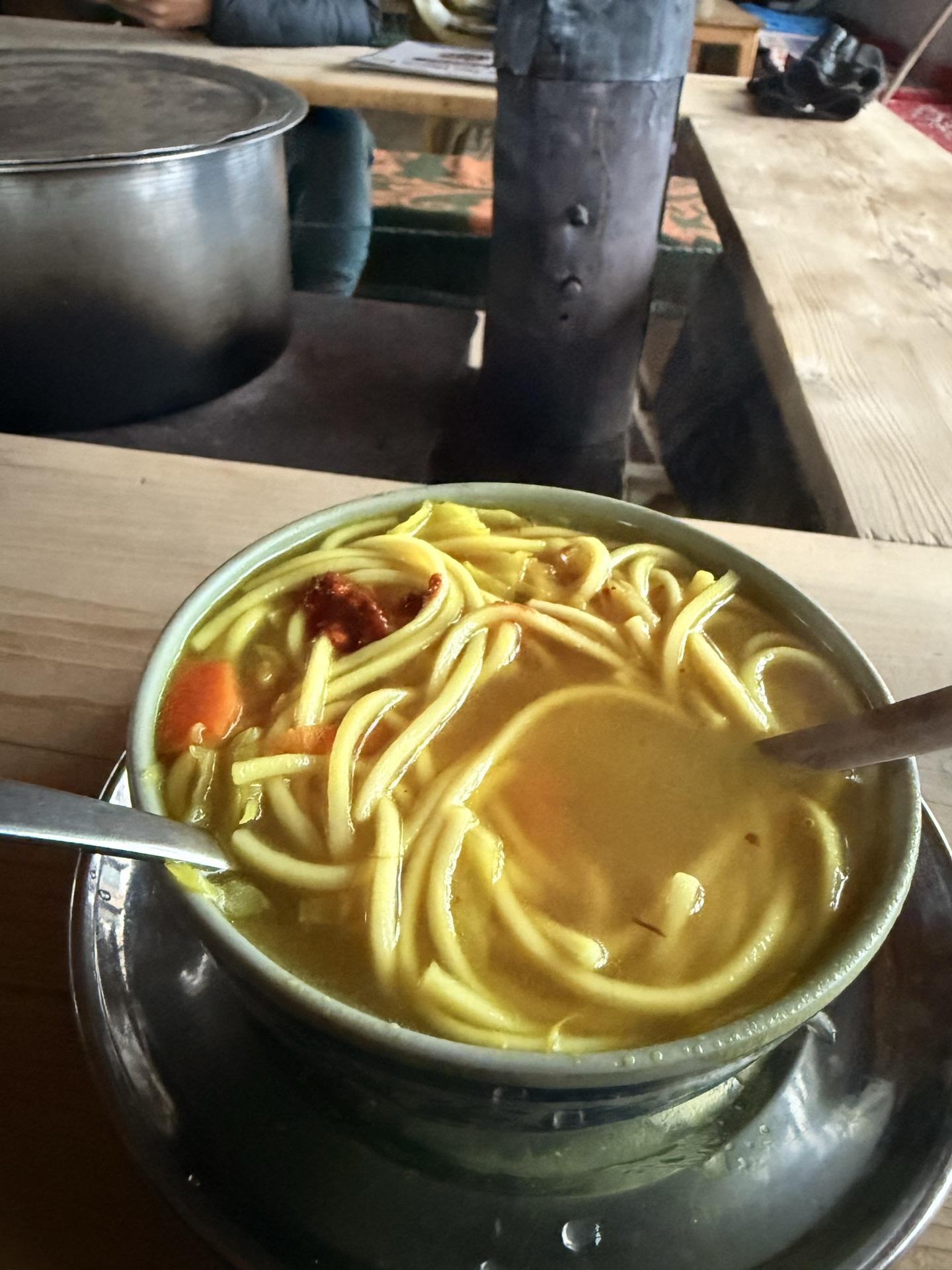 A steaming steel bowl of thukpa on a wooden table
