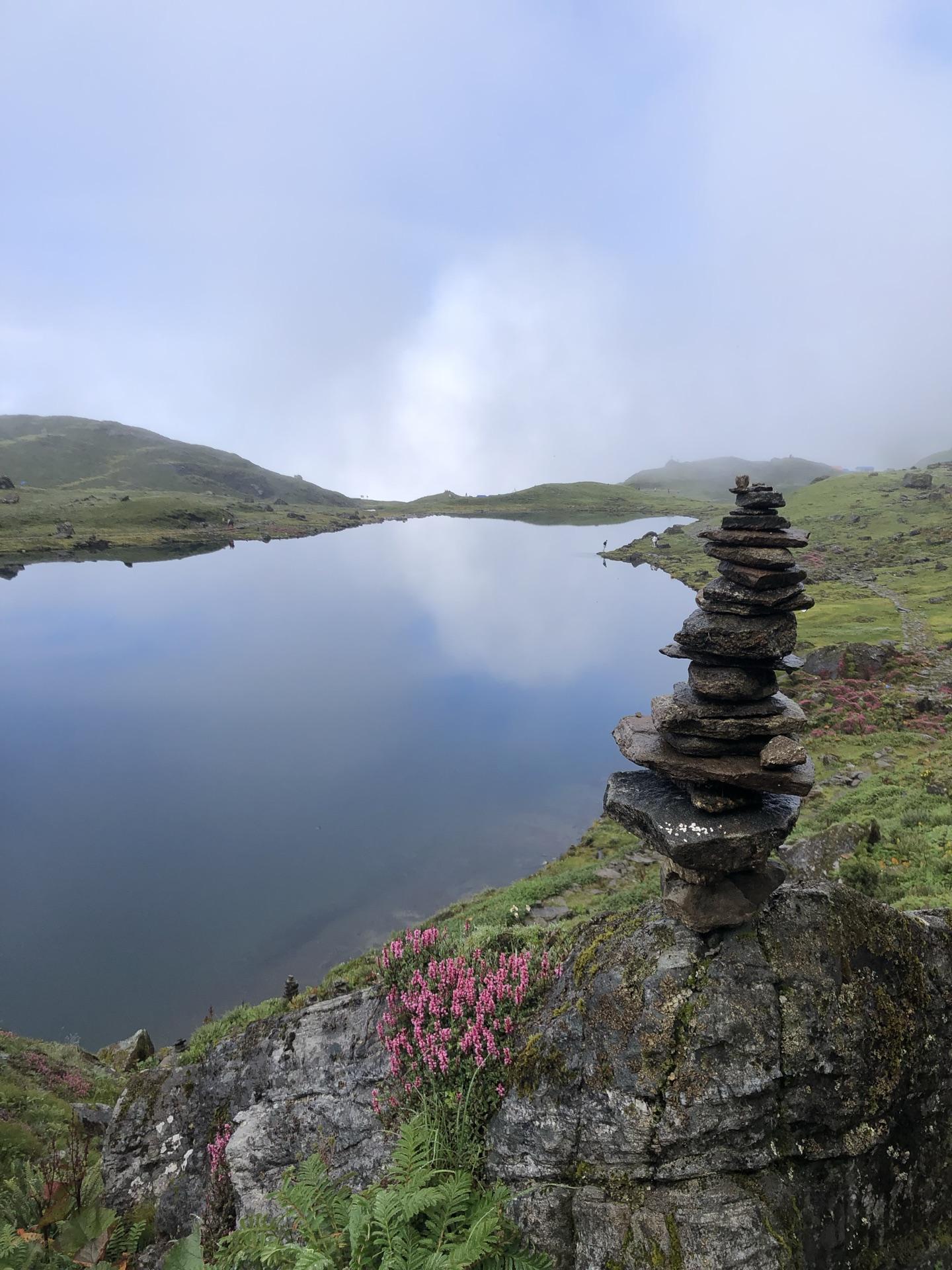 A stacked stone cairn at the lakeshore, pink bloom and still water behind