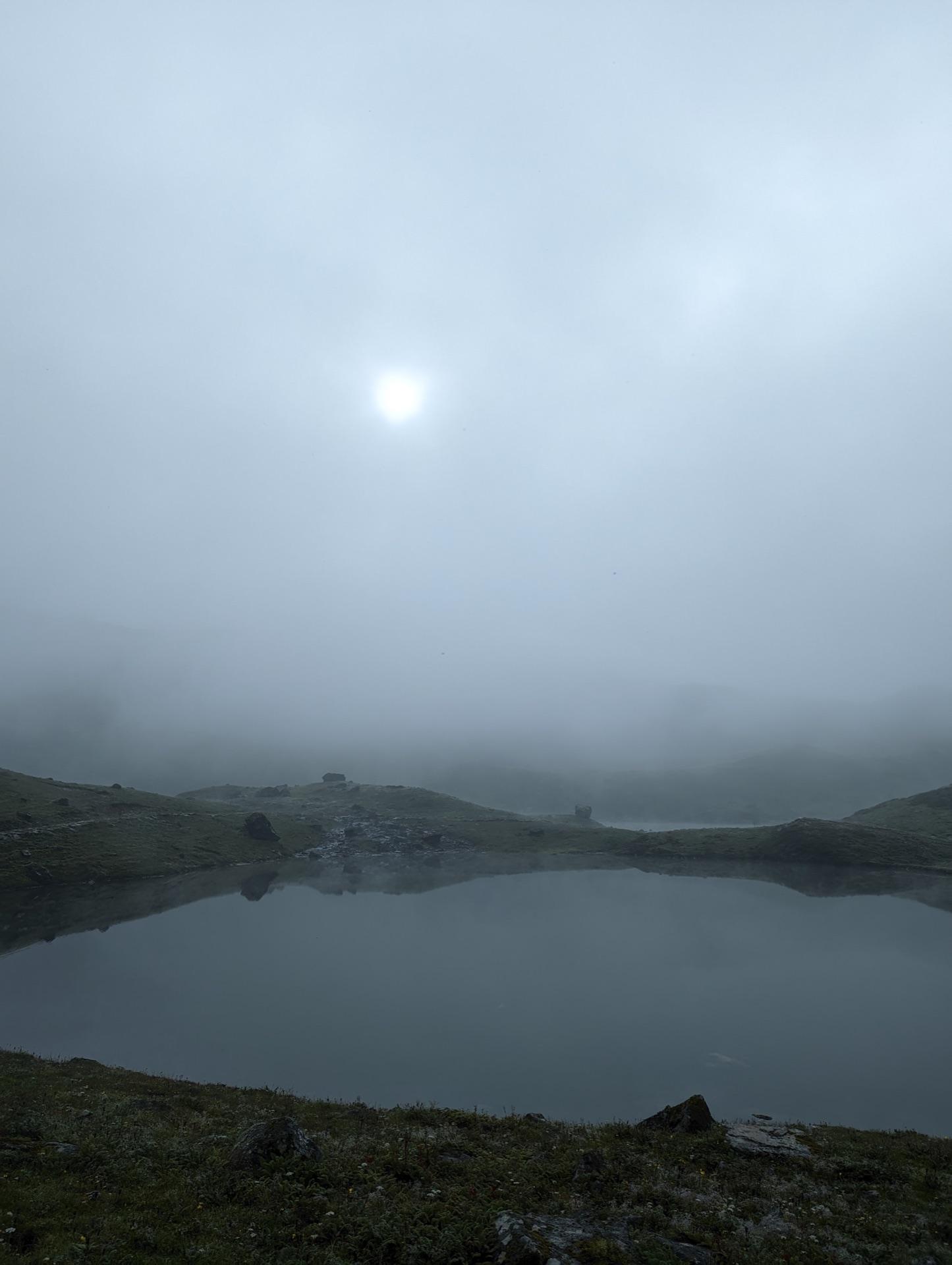 The sun as a pale disc burning through fog above the lake