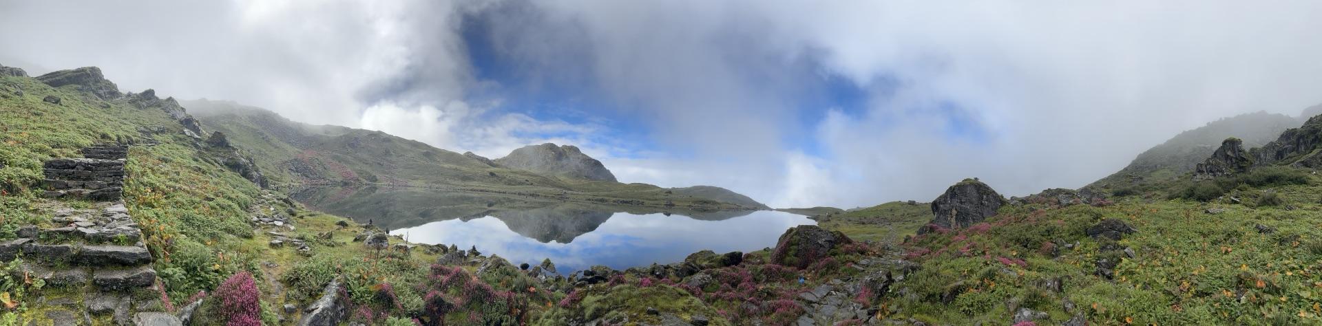 Wide panorama of the mirror-still lake reflecting the hills and clearing sky