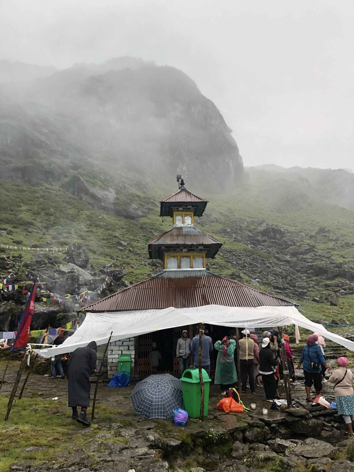The small pagoda temple at the lakeshore with tarps and early pilgrims in mist