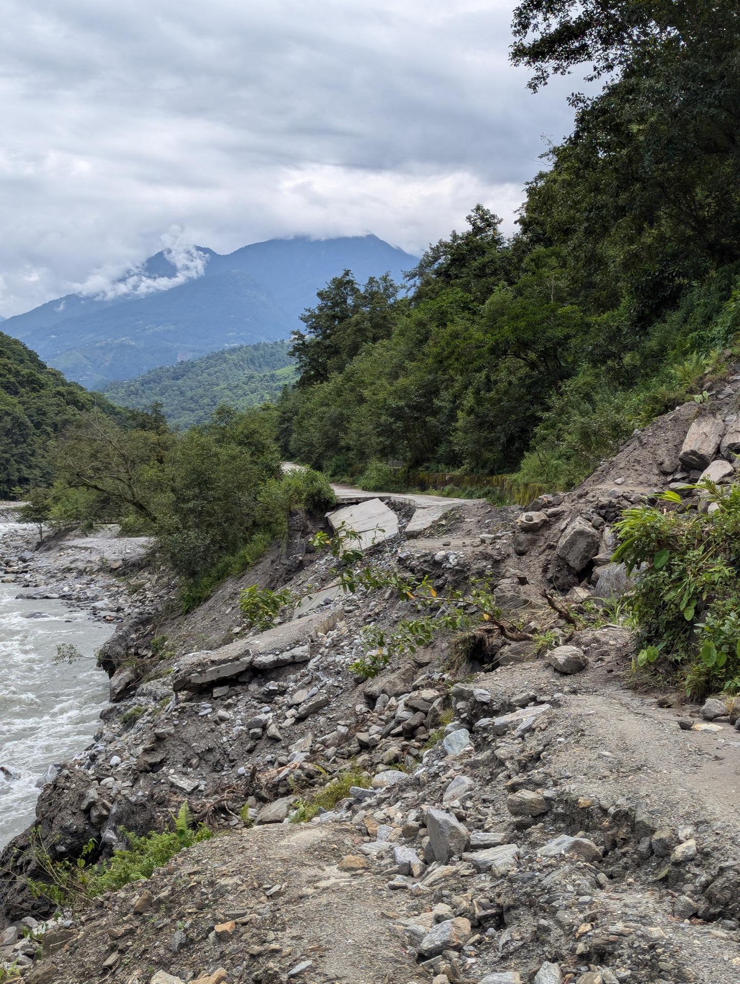 A hill road washed out by monsoon rain, its edge collapsed toward the river