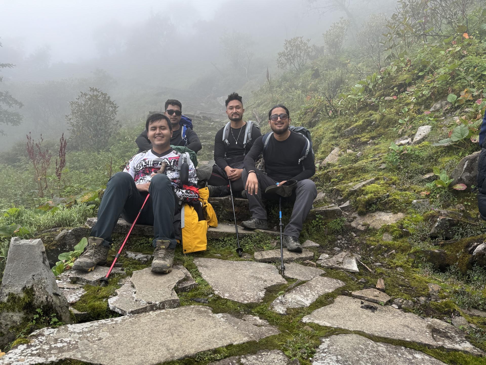The group resting on mossy rocks beside the trail in mist