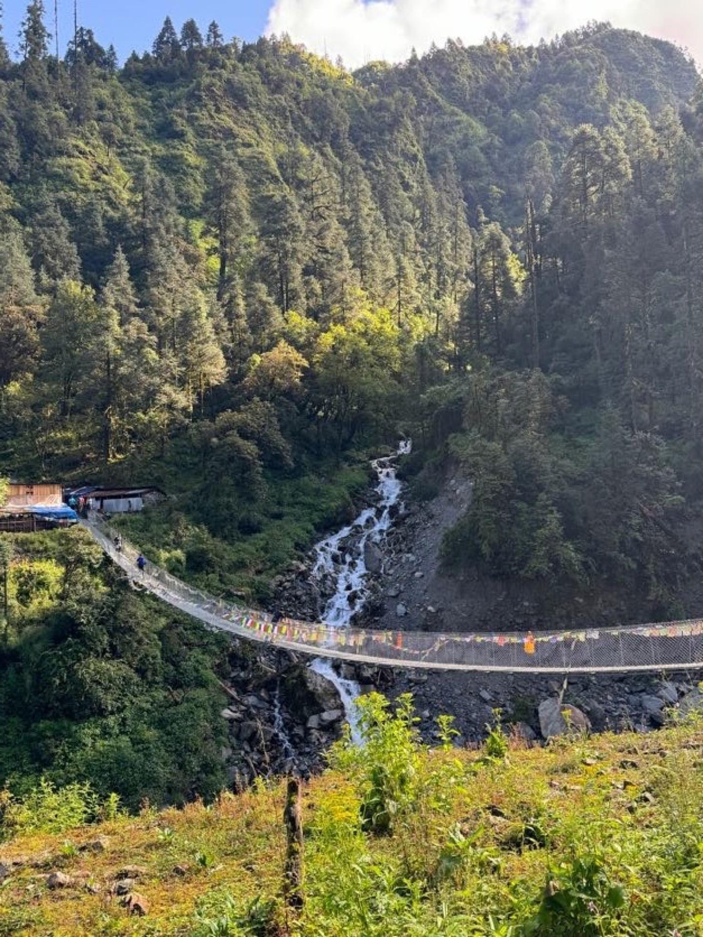 The suspension bridge from above, spanning the gorge below a waterfall