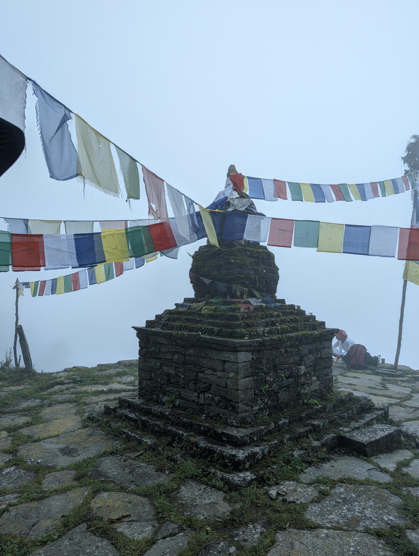A stone chorten wrapped in prayer flags in thick mist