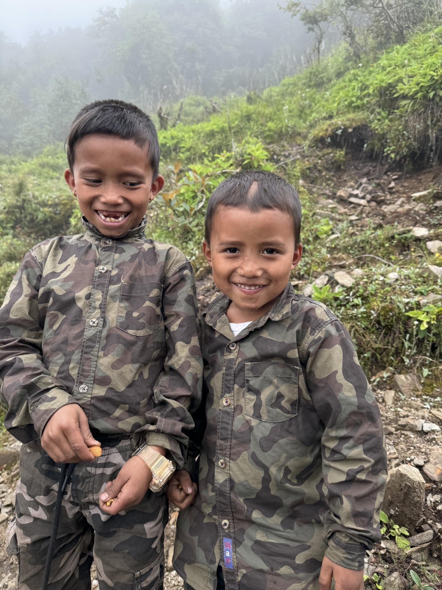 Two village kids grinning at the camera beside the trail
