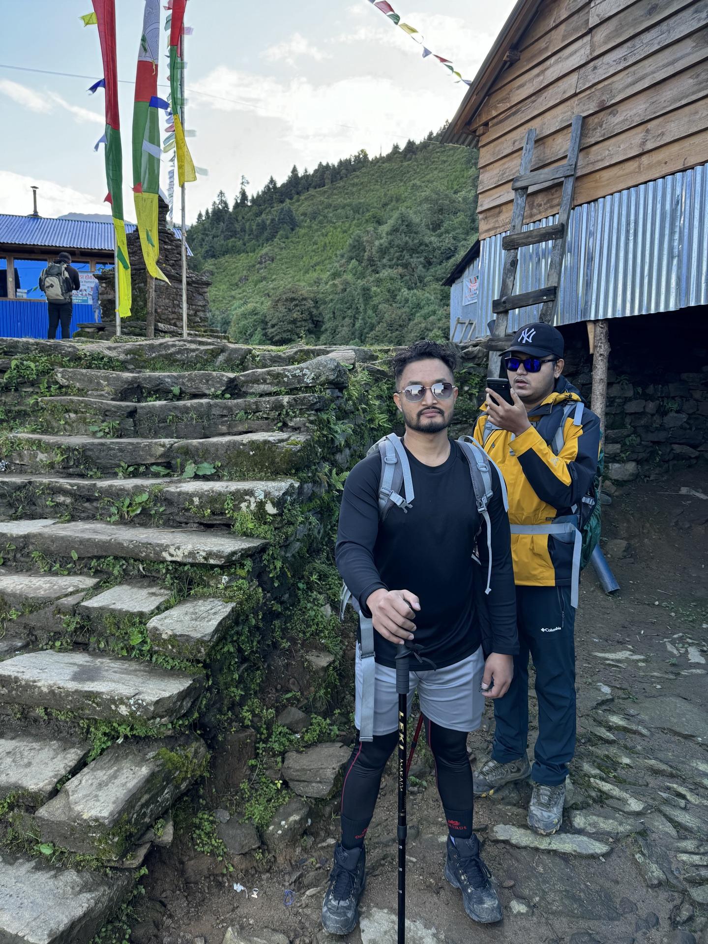 Two of us with packs and poles below the teahouse, prayer flags overhead