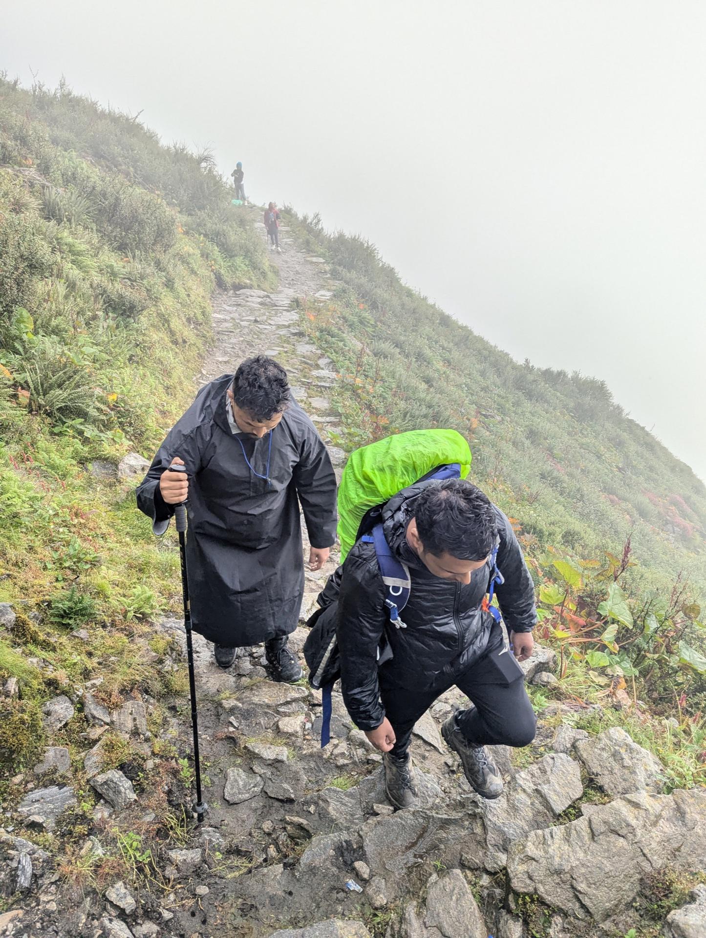 Two of us in rain gear climbing the steep grass slope in mist