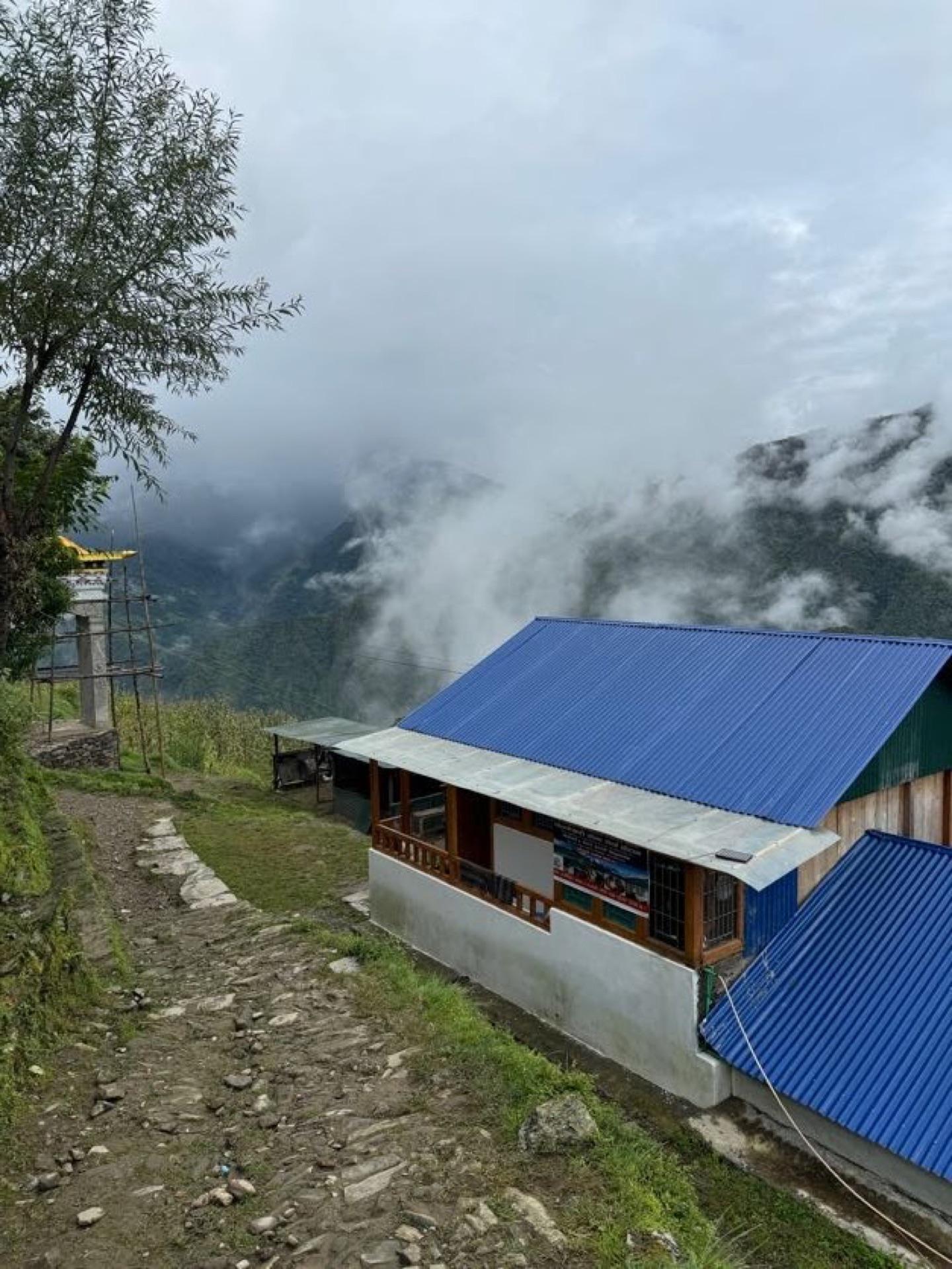 A blue-roofed teahouse perched on a green hillside above a sea of cloud